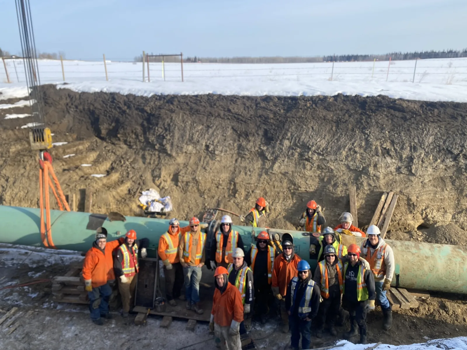 Midwest field crew gathered beside a pipeline at a winter work site