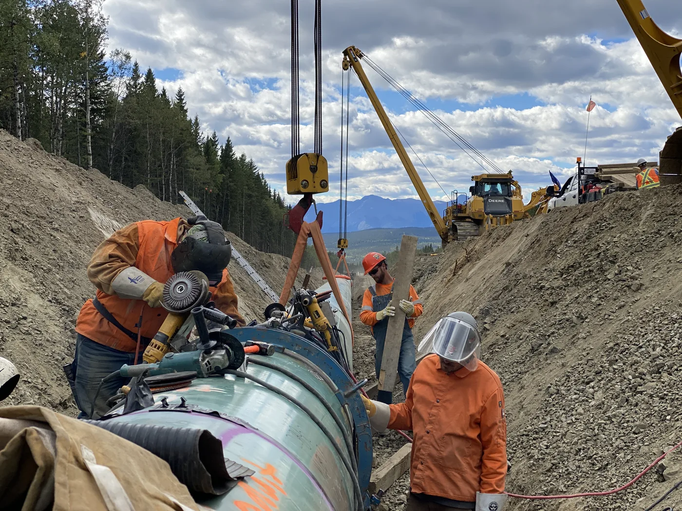 Midwest crew members preparing a pipeline joint with equipment in a mountain work area