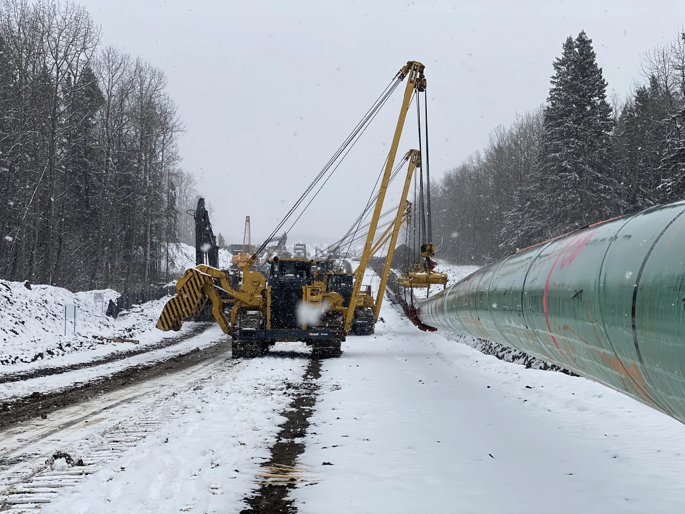Pipelayers and pipe in a snow-covered construction corridor