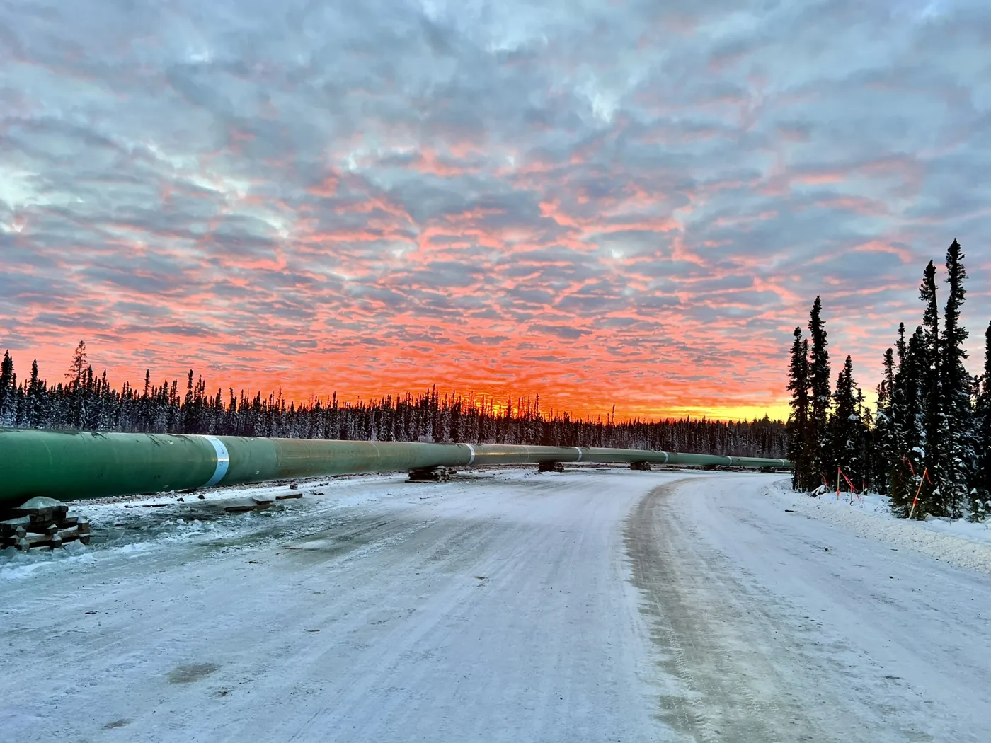 A pipeline laid out in a snow-covered construction corridor at sunset